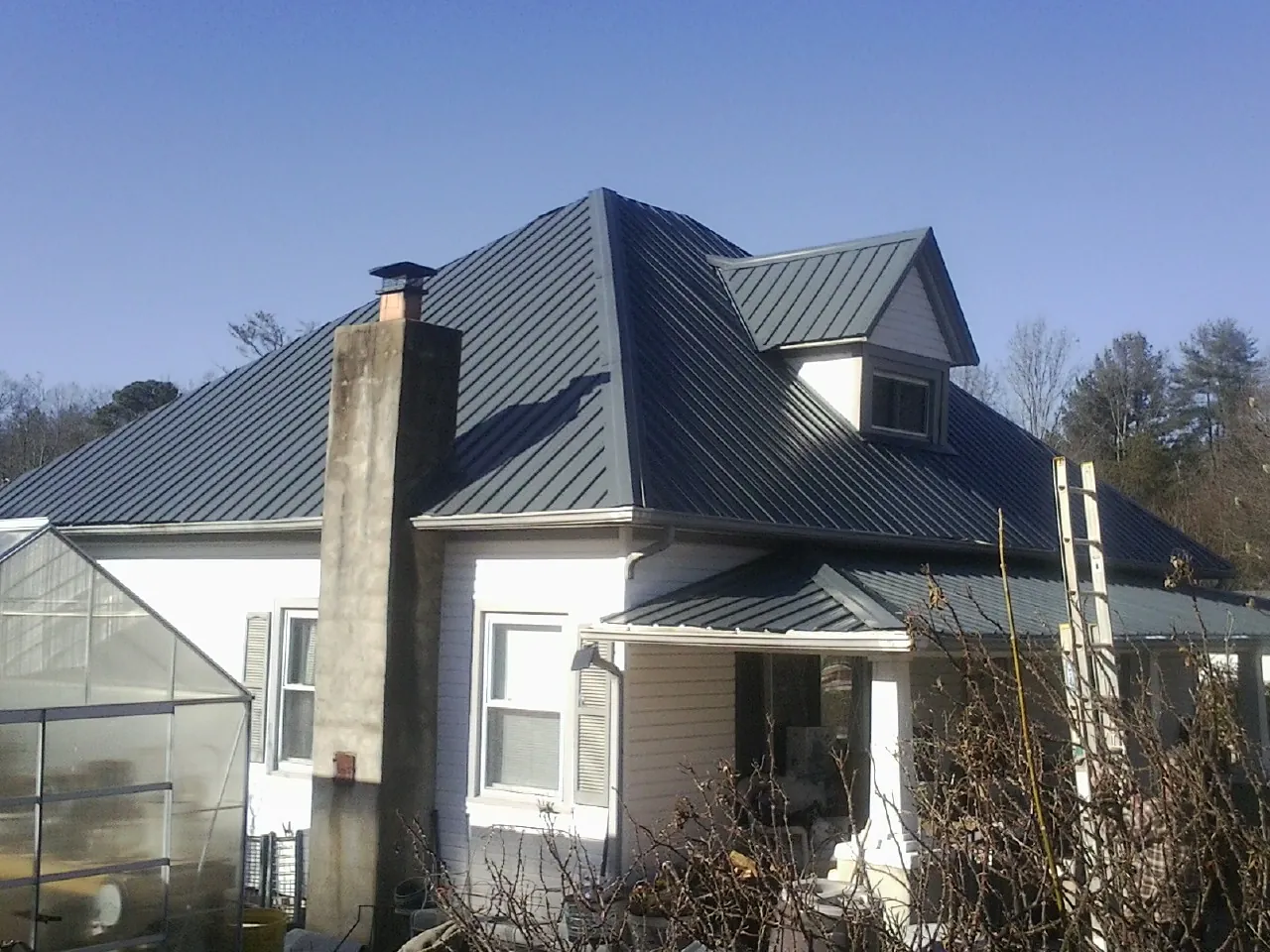 Dark blue standing seam metal roof on a white farmhouse with dormer — Slate & Tile Roof Repair by Roofing Brothers in Divide