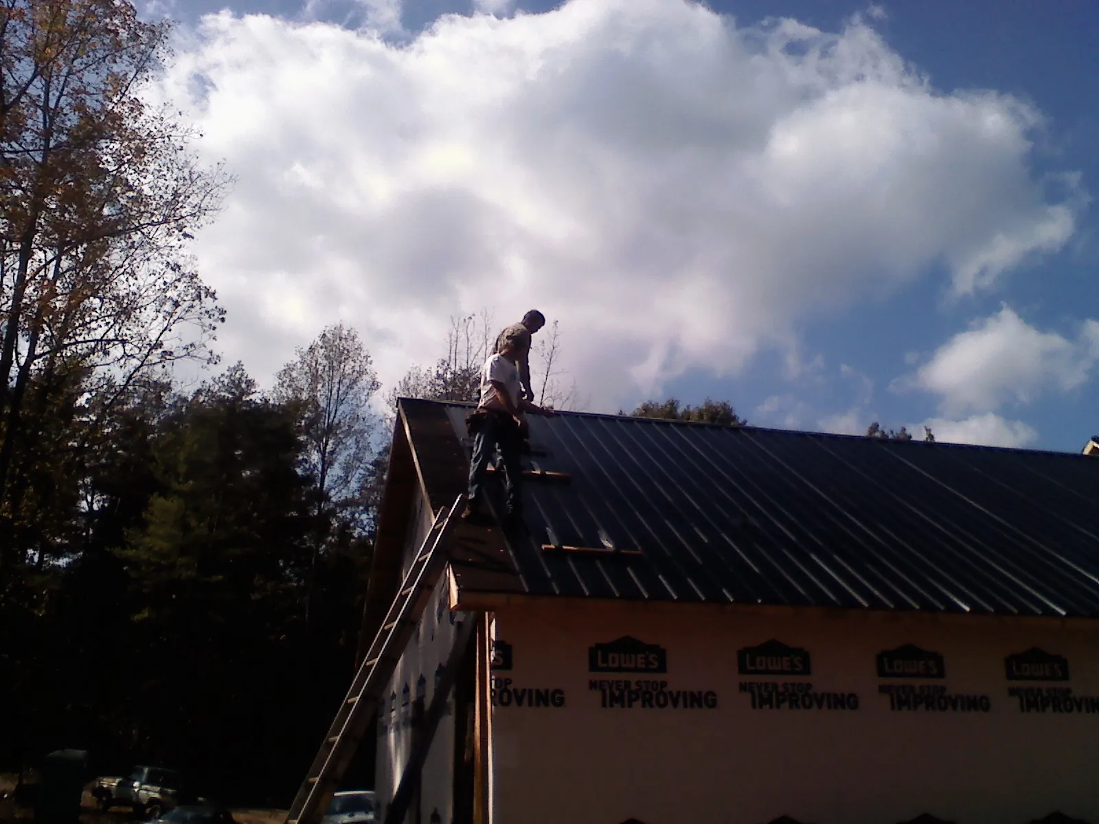 Roofer fastening dark metal panels high against a cloudy sky, from a Roof Inspection job in Divide